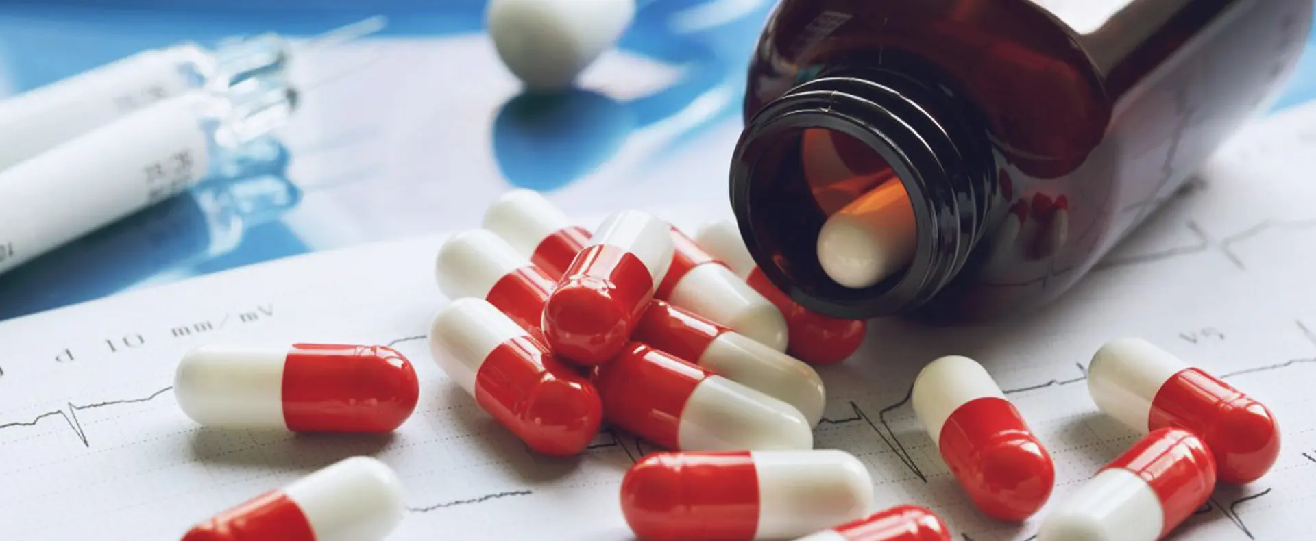 Red and white capsule pills scattered with a medical chart in the background