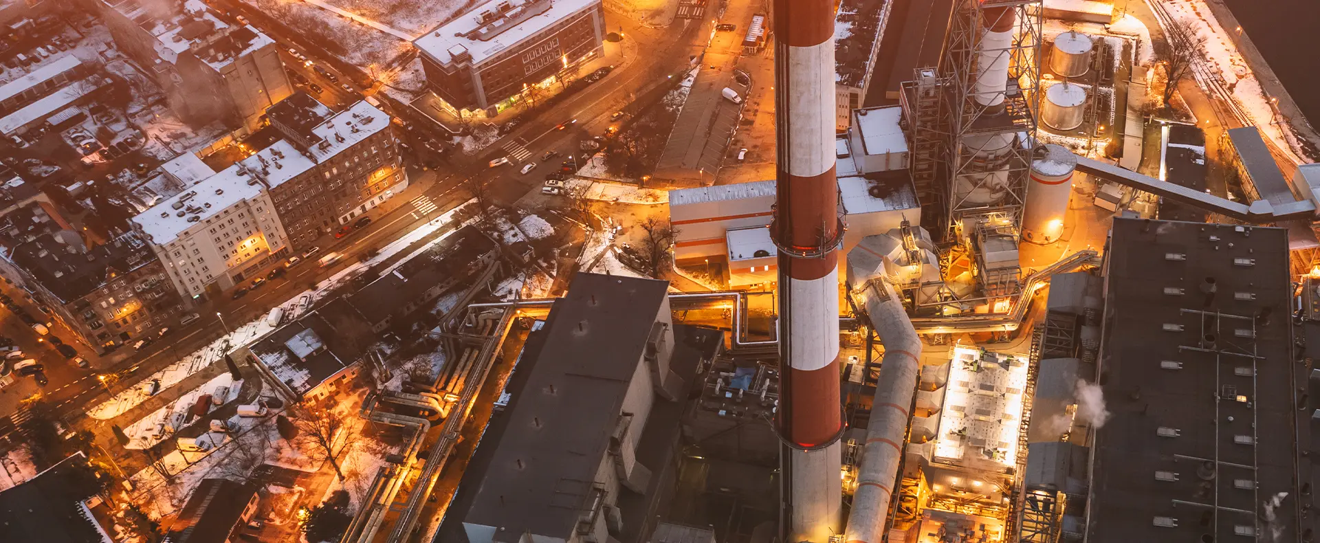 An industrial power plant with a striped smokestack at night in a city