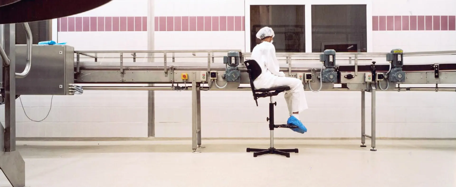 A worker in front of a conveyor belt A worker in a white protective suit monitoring a conveyor line in a pharmaceutical facility