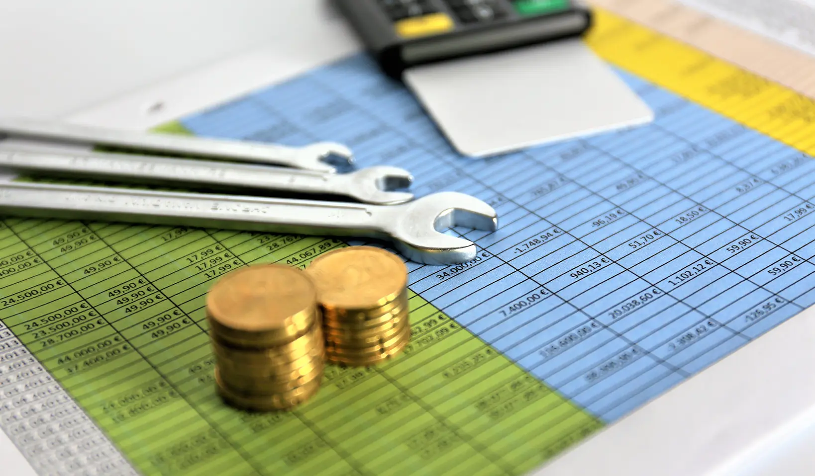 A calculator, stacked coins, and wrenches on top of a spreadsheet, symbolizing operating expenses (OPEX).