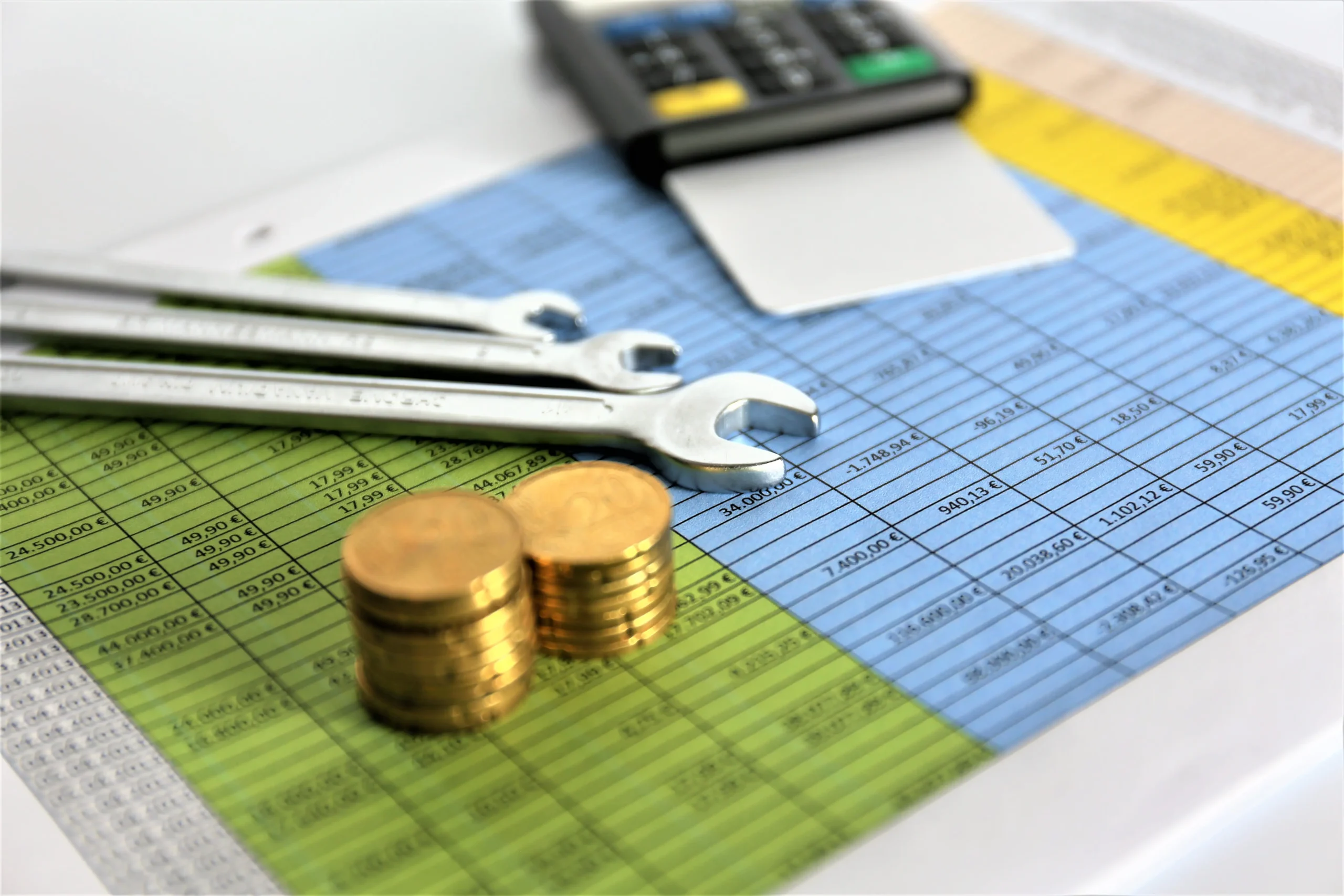 A calculator, stacked coins, and wrenches on top of a spreadsheet, symbolizing operating expenses (OPEX).
