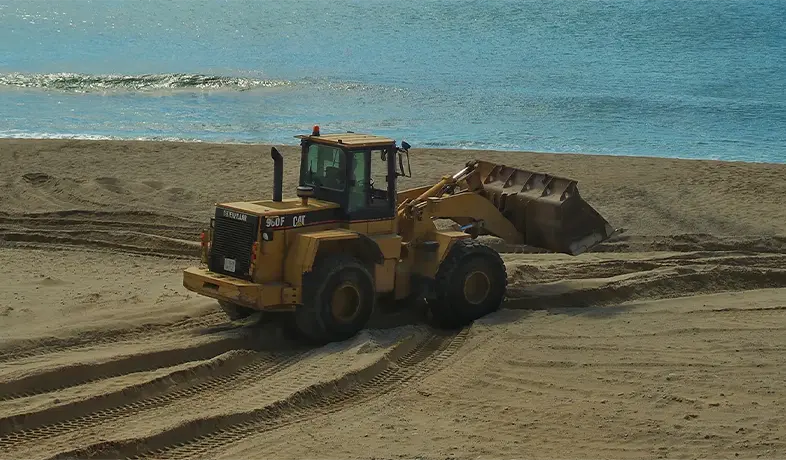 yellow bulldozer on beach, moving across the sand