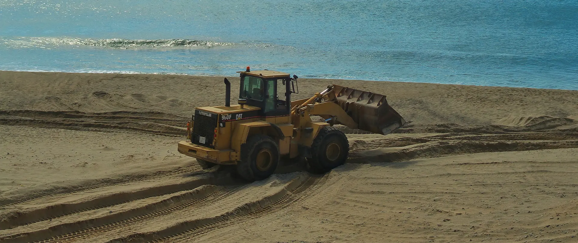yellow bulldozer on beach, moving across the sand
