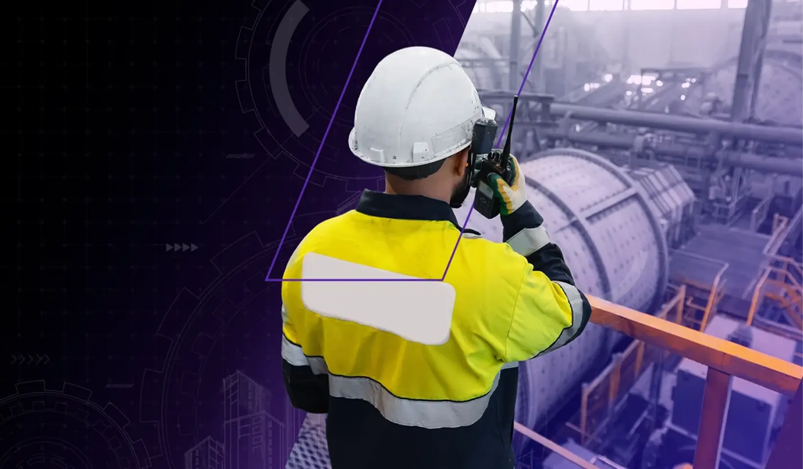 A factory worker wearing a safety helmet and a yellow jacket communicates through a handheld radio to monitor a manufacturing plant